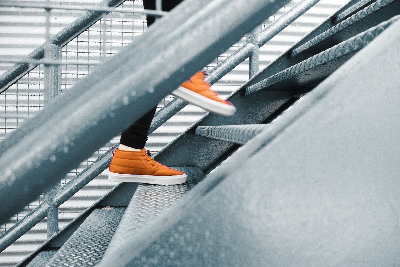 Person in orange sneakers walking up a metal staircase